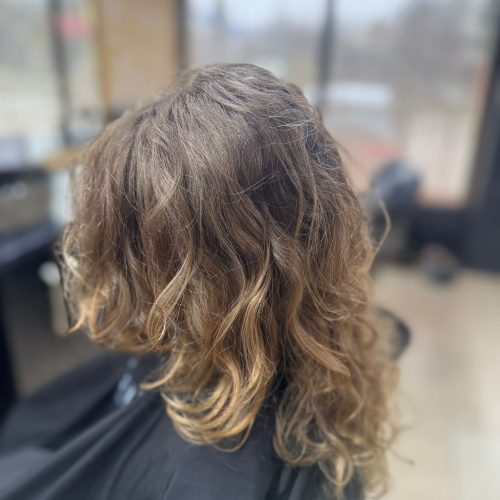 Vedere din spate a unei tunsori pentru femei cu bucle lejere si naturale, par castaniu deschis cu reflexe blonde aurii la vârfuri si volum, realizata la Sia's Beauty Iasi, Lunca Cetatuii.