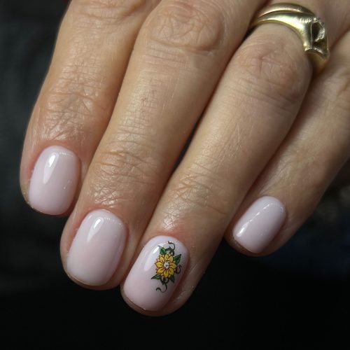 Manichiura milky white pe unghii scurte si rotunde cu floare decorativa pe degetul inelar, design delicat si elegant