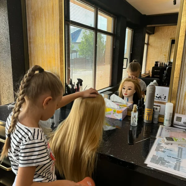 Anastasia, fiica patronilor salonului Sia's Beauty Center din Iasi, Lunca Cetatuii, surprinsa in timp ce piaptana un cap de manechin la blatul salonului. In oglinda se reflecta interiorul elegant al salonului, cu produse profesionale de ingrijire a parului aranjate pe blatul negru.